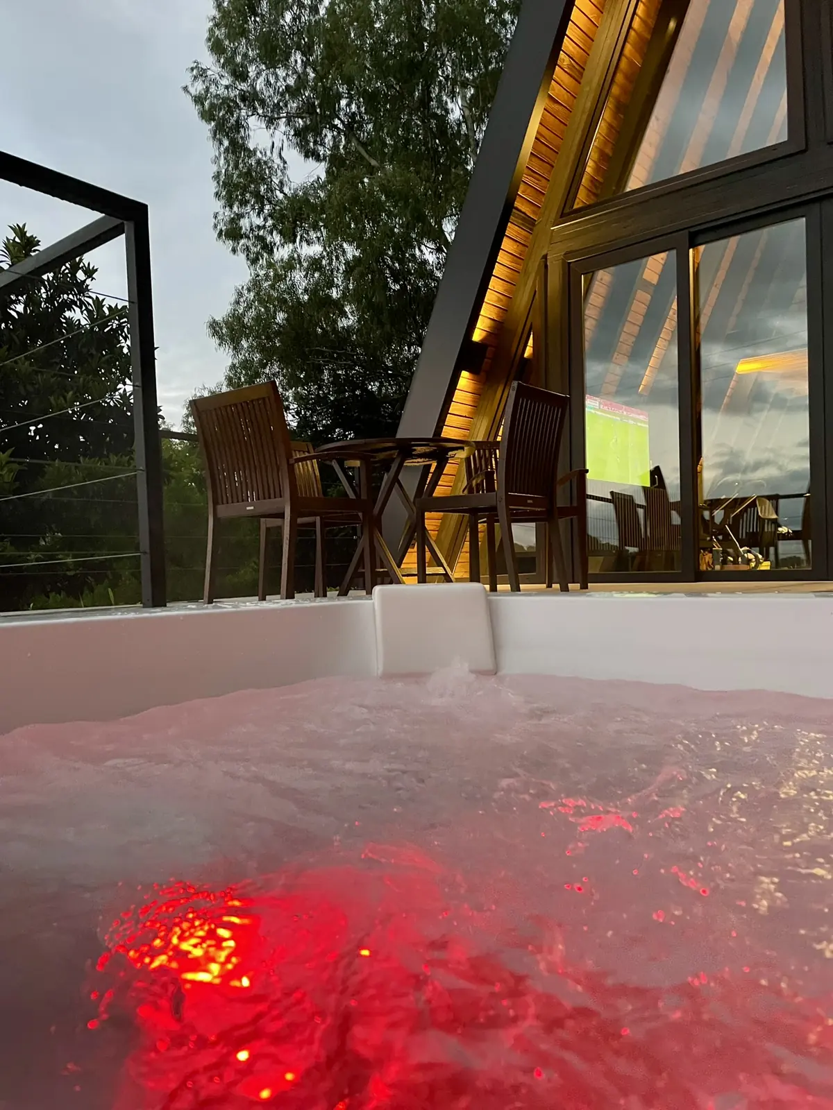Jacuzzi à noite com luz de cromoterapia vermelha e a cabana iluminada